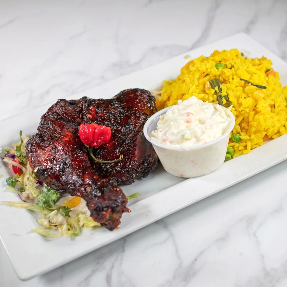 Glazed grilled chicken with a red pepper garnish, yellow rice, creamy coleslaw, and salad on a rectangular white plate.