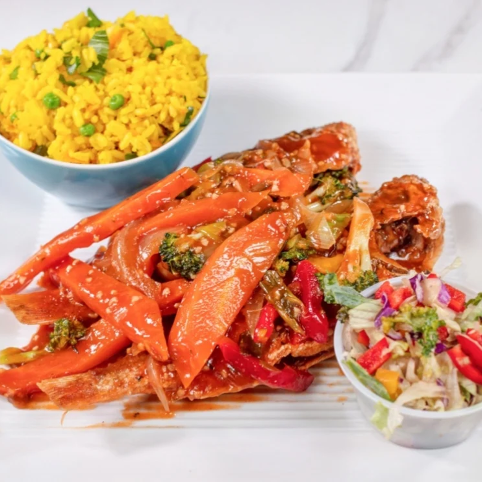 Plate of saucy roasted vegetables with broccoli and peppers, served with yellow rice and a colorful side salad.
